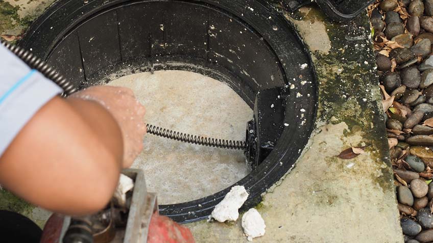 Plumber repairing clogged grease trap with auger machine