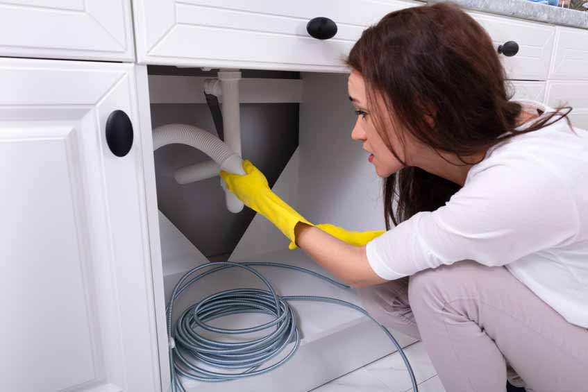 Woman cleaning clogged pipe under kitchen sink