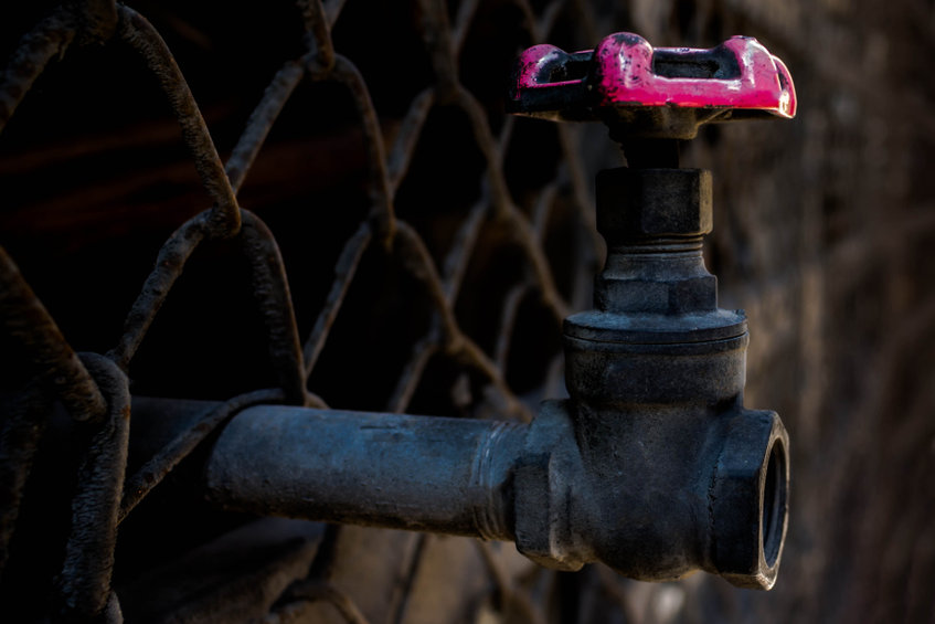 Rusty water valve and pipe outside a building