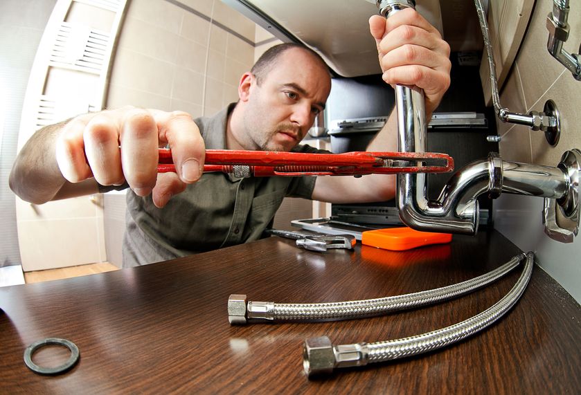 Plumber at work under sink fixing pipes