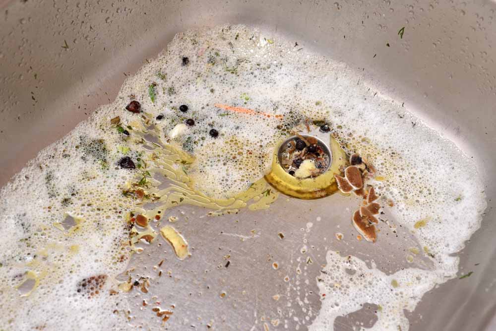 Dirty kitchen sink with foam and scraps after washing dishes