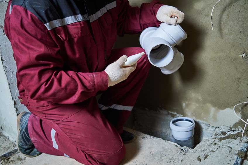 Plumber installing plastic sewage pipe fitting at construction site