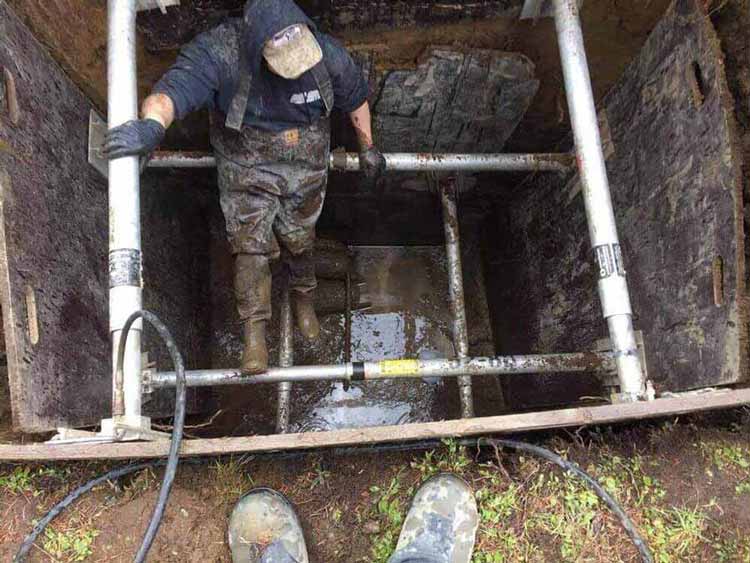 Sewer repair technician climbing into large pit to repair pipes