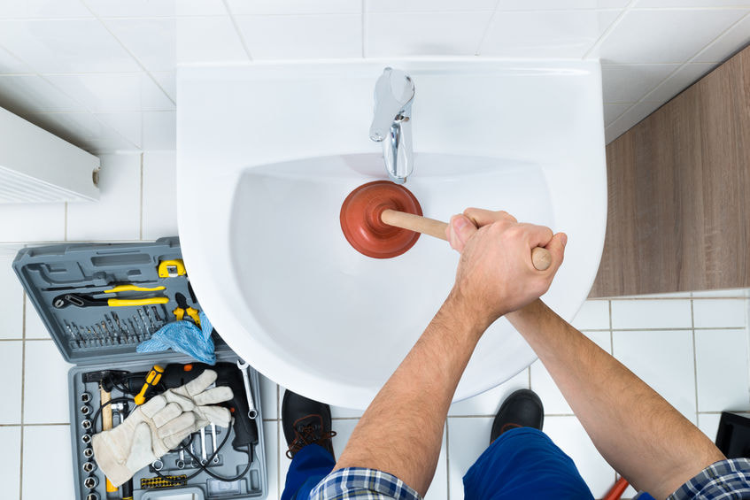 Overview of man holding plunger trying to unclog bathroom sink