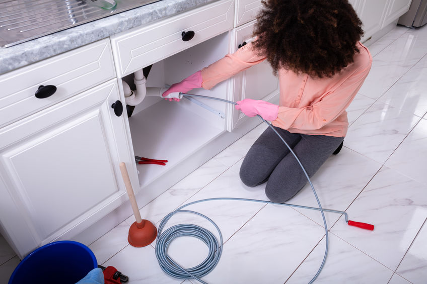 Woman cleaning clogged sink pipe in kitchen