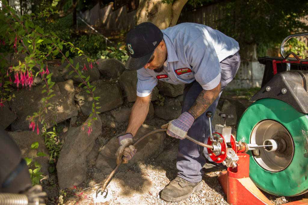 Plumbing technician snaking a sewer line outdoors