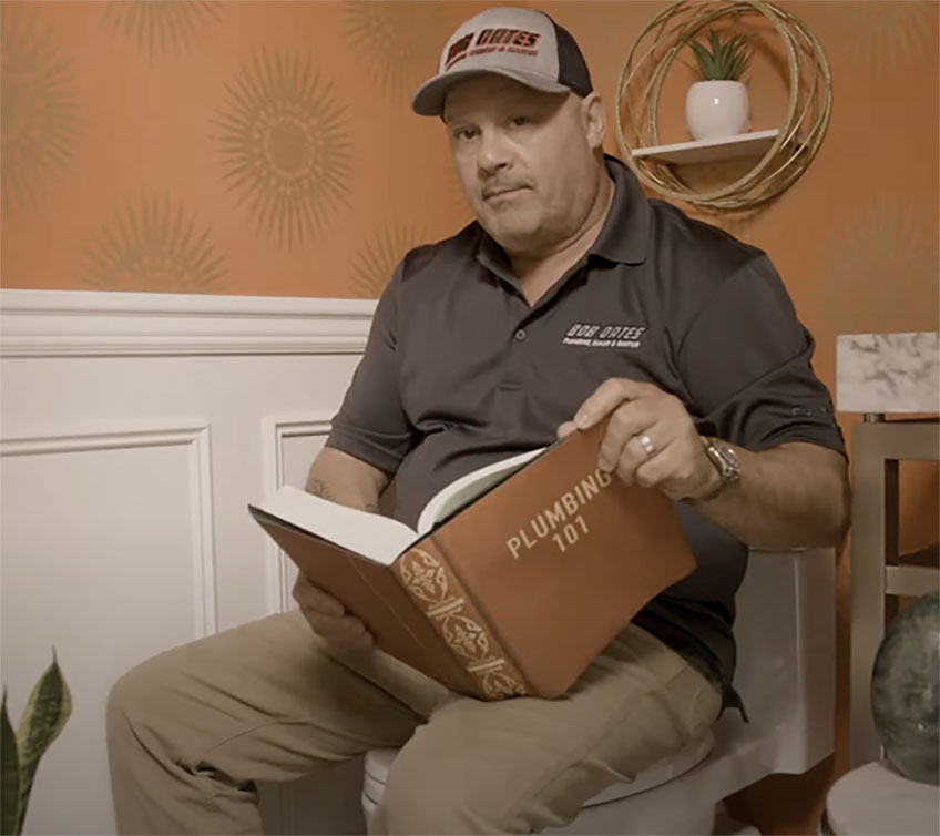 Technician in bathroom with a book that says "Plumbing 101" on cover