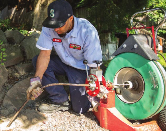 Plumbing technician snaking a sewer line outdoors