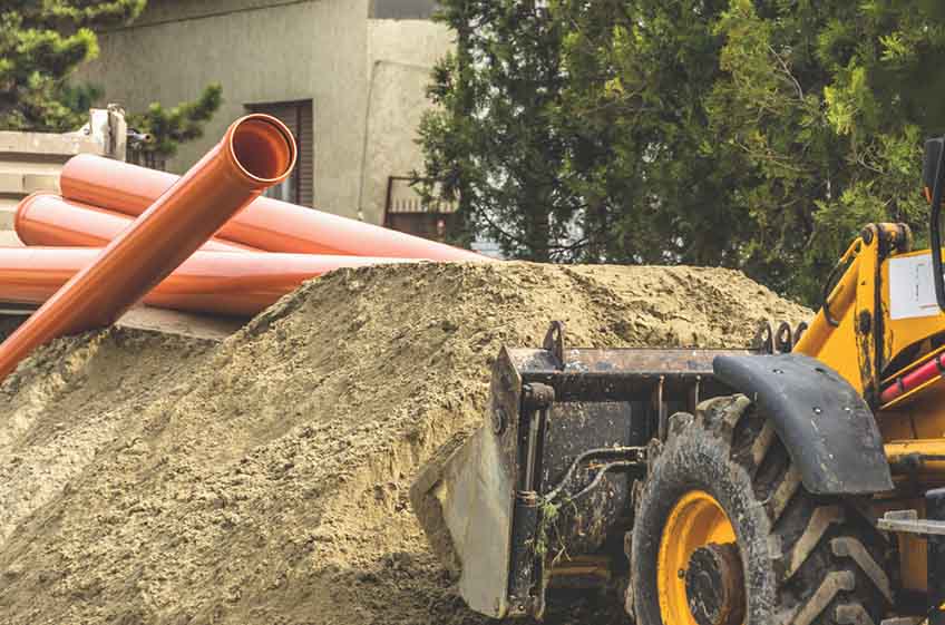 Bulldozer in front of large pile of dirt and stacked sewer pipes