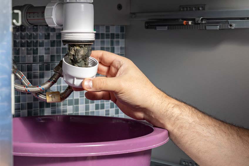 Plumber removing blockage in pipes under sink