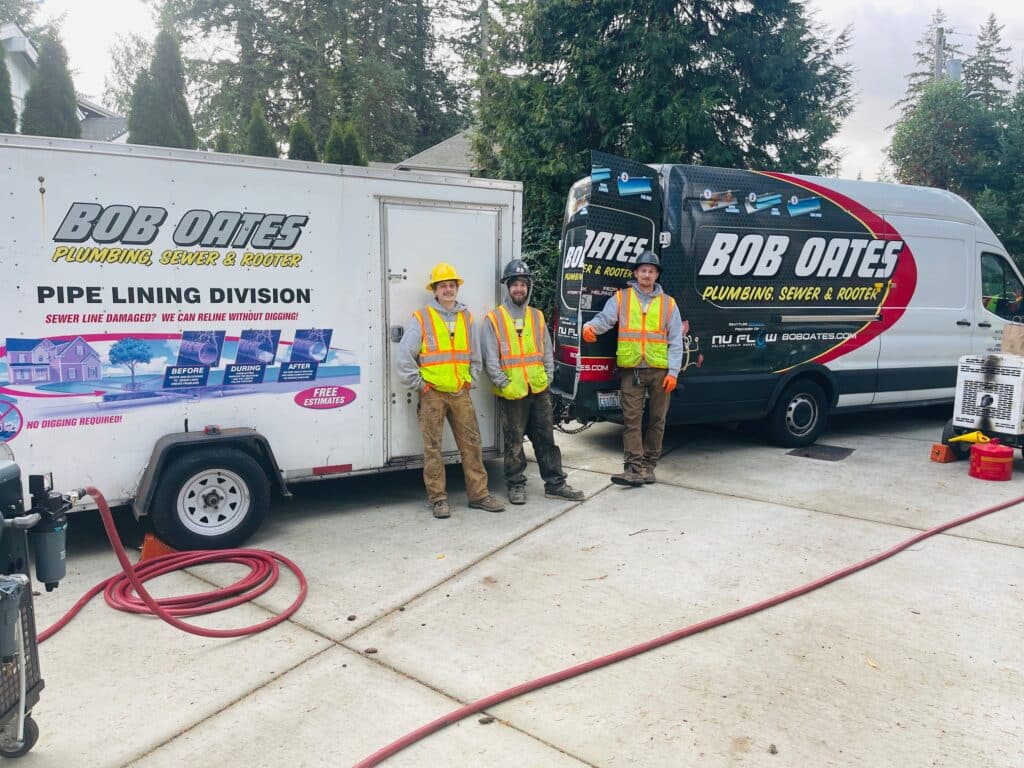 Two Bob Oates work trucks in the driveway at a sewer pipe relining job. Three technicians are standing in front looking toward the camera, about to go to work.