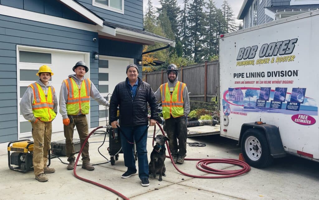 Owner Bob Oates standing with his plumbing crew and company service dog in front of a Bob Oates Plumbing, Sewer & Rooter truck during a residential drain cleaning service in the Seattle area.