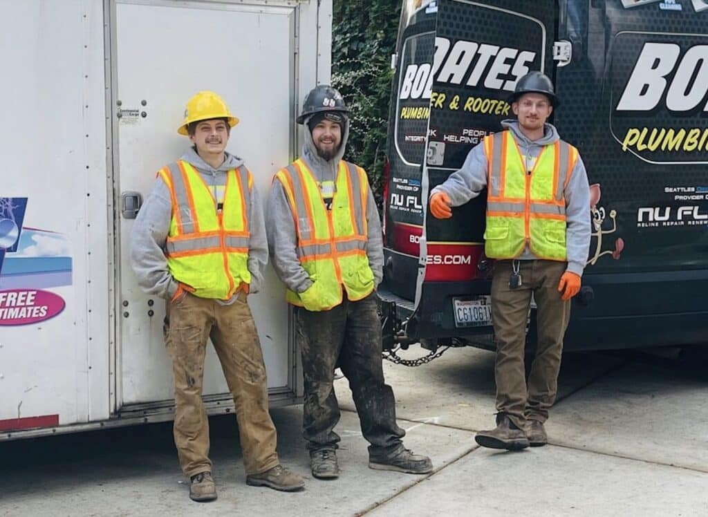 Three Bob Oates Plumbing, Sewer & Rooter technicians standing beside company service vehicles during a residential service call in the Seattle area.
