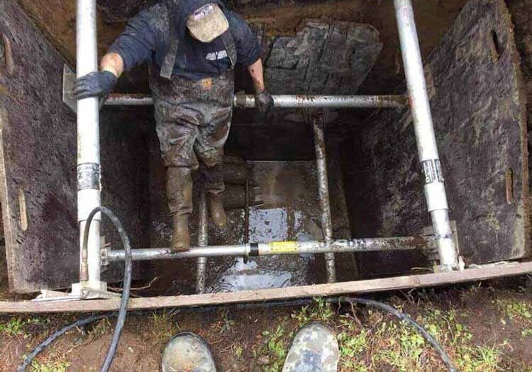Sewer repair technician climbing into large pit to repair pipes