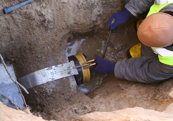 Sewer technician working on sewer line inside of dug out trench