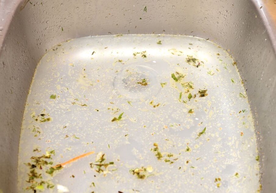 Standing water and food debris in a kitchen sink due to a clogged drain.